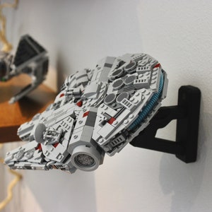 May include: A white and grey Lego Millennium Falcon spaceship model mounted on a black wall mount. The model has red and blue details.