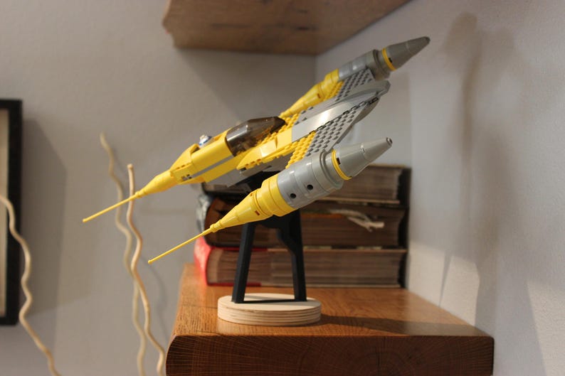 May include: A yellow and gray Lego Star Wars V-4X-D starfighter model on a black stand. The model is on a wooden surface.