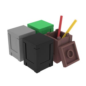 May include: A collection of four square storage containers in gray, green, black, and brown. The brown container is open with a detached lid nearby, holding one red pencil and one yellow pencil inside its hollow, block-like structure.