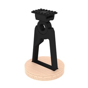 May include: Black plastic phone stand with a gear design and a flat top. The stand is mounted on a round wooden base.
