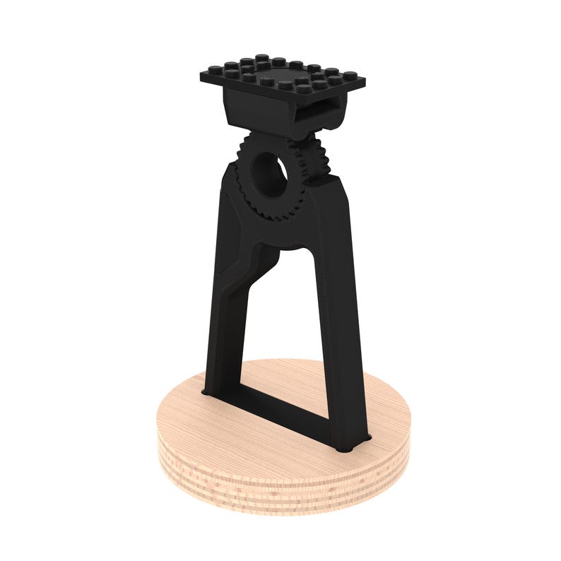 May include: Black plastic phone stand with a gear design and a flat top. The stand is mounted on a round wooden base.