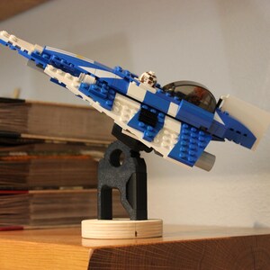 May include: A blue and white Lego spaceship model on a black stand. The spaceship has a white cockpit and a blue body with white stripes.