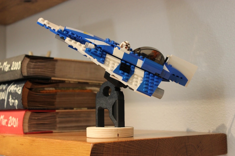 May include: A blue and white Lego spaceship model on a black stand. The spaceship has a white cockpit and a blue body with white stripes.