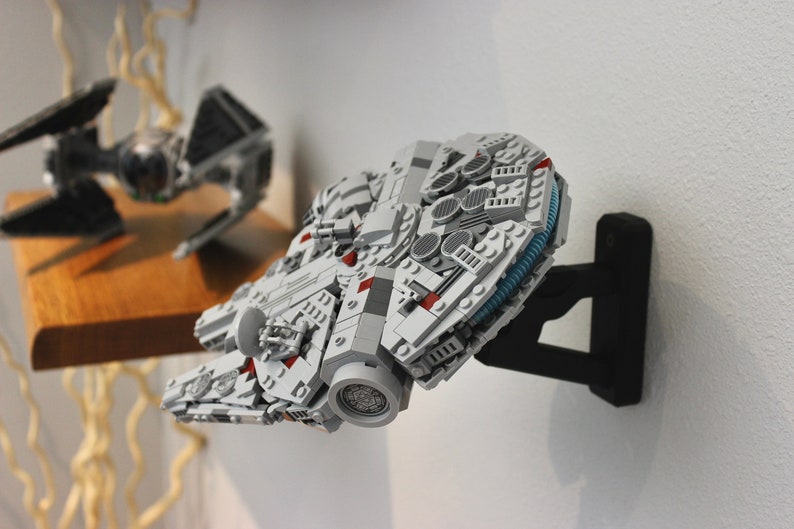 May include: A white and grey Lego Millennium Falcon spaceship model mounted on a black wall mount. The model has red and blue details.