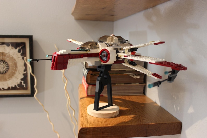 May include: A red and white Lego spaceship model with a black stand. The spaceship has a red cockpit and white wings. The stand is made of black plastic and has a round base.