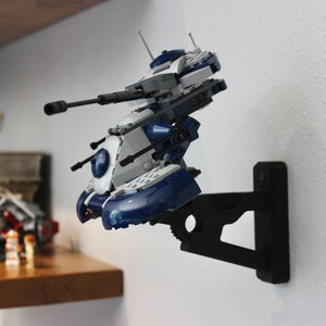 May include: A blue and white Lego Star Wars vehicle mounted on a black wall mount. The vehicle has a large cannon and is in a flying position.