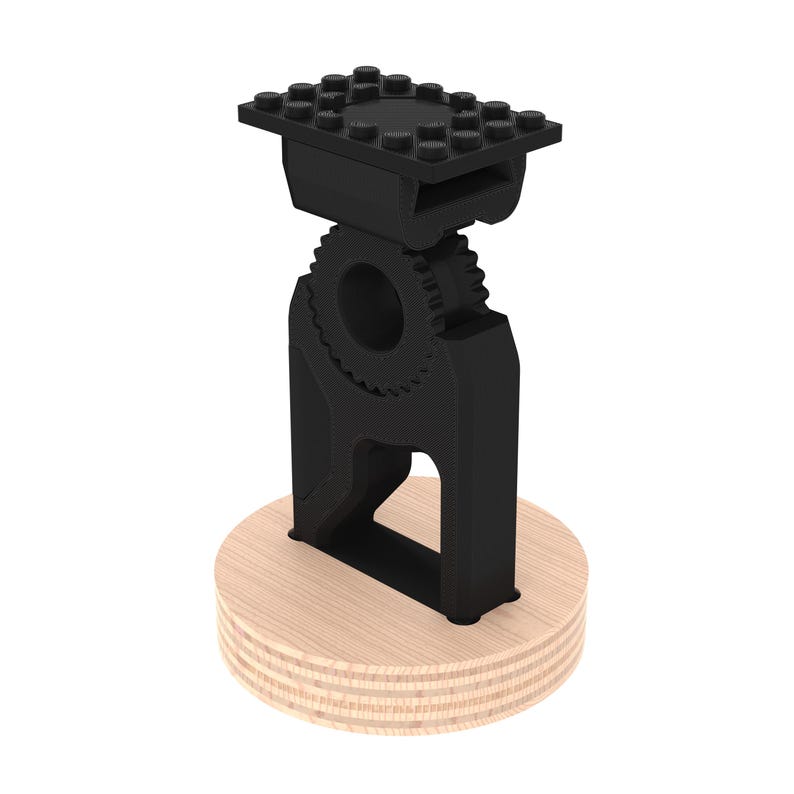 May include: A black 3D printed phone stand with a gear design and a lego-style top plate. The stand is mounted on a wooden base.
