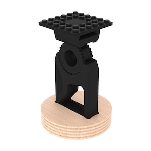 May include: A black 3D printed phone stand with a gear design and a Lego-style base. The stand is mounted on a wooden base.
