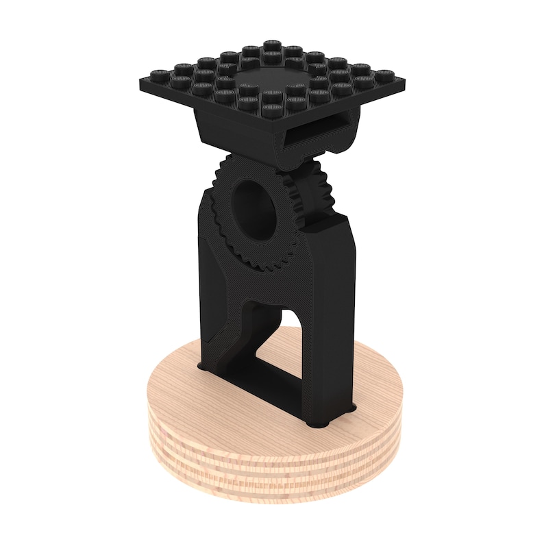 May include: A black 3D printed phone stand with a gear design and a Lego-style base. The stand is mounted on a wooden base.