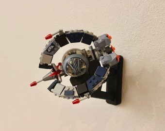 May include: A gray and blue Lego spaceship with red accents, mounted on a black stand. The spaceship has a clear dome in the center and is designed to look like a Star Wars ship.