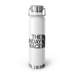 May include: A white insulated water bottle with a silver lid and handle. The bottle features the text "THE SUNDAY RACE" in black, with a stylized mountain graphic. The bottle has a silver base and rim.