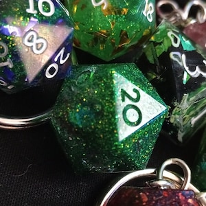 Puede incluir: Primer plano de un llavero con varios dados verdes, negros y rojos con purpurina. Los dados están unidos a una cadena plateada.