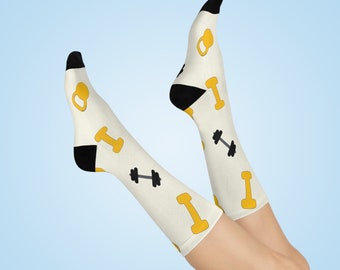 Könnte beinhalten: Ein Paar weiße Socken mit einem schwarzen und gelben Hantel- und Kettlebell-Muster. Die Socken werden an den Beinen einer Person getragen.