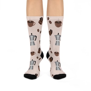 May include: A pair of beige socks with a coffee themed design. The socks feature a repeating pattern of coffee cups, coffee pots, and coffee beans.