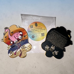 May include: Two custom coins. One coin features a pink flamingo with a life preserver, set against a beach scene. The other coin is black with gold accents and the text "USN". The coins are from Aloha Challenge Coins & Laser Engraving.