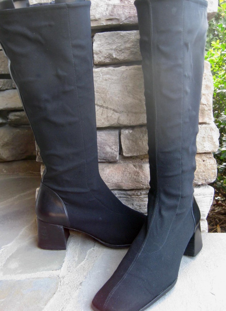 Puede incluir: Un par de botas negras hasta la rodilla con punta cuadrada y tac&oacute;n ancho. Las botas est&aacute;n hechas de una tela el&aacute;stica y tienen un detalle similar al cuero en el tal&oacute;n. Las botas est&aacute;n sobre una superficie de piedra.