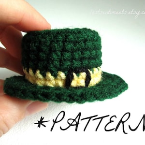May include: A small green crocheted leprechaun hat with a yellow and black band. The hat is being held by a hand.