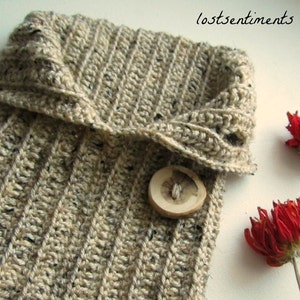 May include: A beige crocheted cowl with a fold-over collar and a wooden button. The cowl is made with a textured stitch and has a speckled appearance.