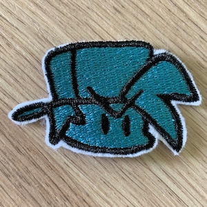 May include: Embroidered patch with a teal and black cartoon design. The patch has a white border and a textured appearance. The design is a stylized face with a black outline. Suitable for clothing or accessories.