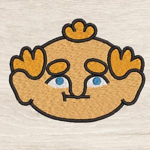 May include: Embroidered cartoon face with a light brown complexion, blue eyes, and a small smile. The face has yellow hair and is outlined in black. The design is on a light beige fabric.