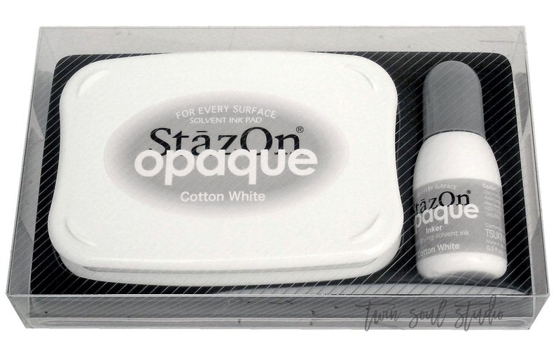 Pu&ograve; includere: Una scatola di plastica trasparente contenente un tampone d'inchiostro bianco e una bottiglia di inchiostro StazOn opaco bianco. Il tampone d'inchiostro ha la scritta "StazOn opaque Cotton White" stampata su di esso. La bottiglia di inchiostro ha la scritta "StazOn opaque Inker solvent ink Cotton White" stampata su di essa.