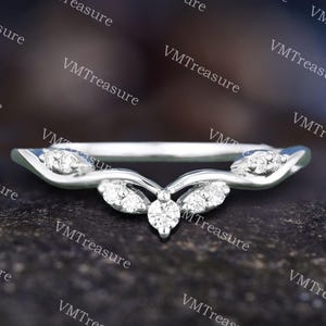 May include: A silver-toned ring with a curved design, featuring a central cluster of small, clear gemstones and additional gemstones along the band. The ring has a delicate, elegant appearance, suitable for special occasions.