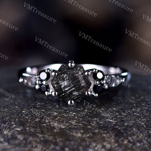 May include: A silver ring with a large, faceted, black gemstone surrounded by smaller black gemstones. The ring is set on a dark, textured surface.