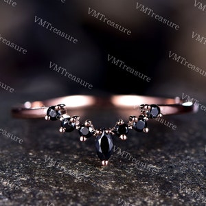 May include: A delicate rose gold ring featuring a marquise-shaped black diamond at its centre, flanked by smaller black diamonds. The ring is displayed against a dark backdrop.
