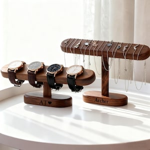 May include: Two wooden display stands. One holds four watches with leather straps. The other holds necklaces. The stands are brown with personalized text at the base. The watches have gold and silver watch faces.