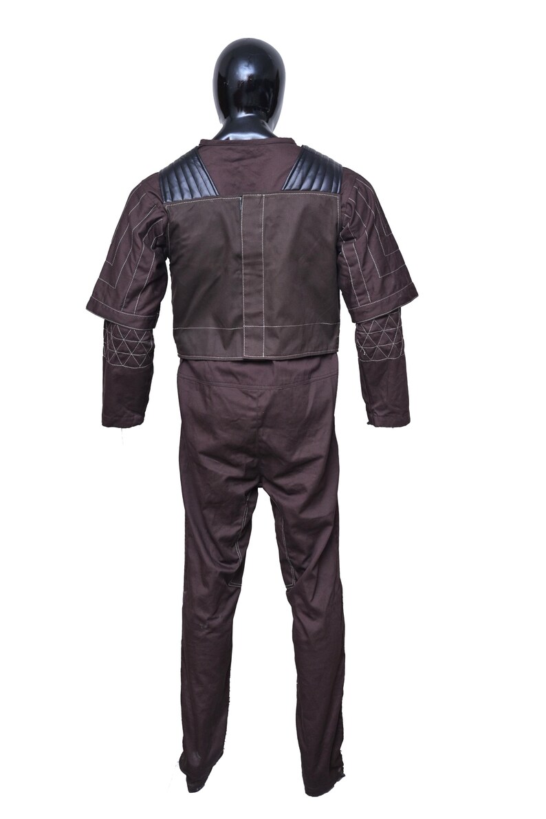 May include: A brown jumpsuit with a black vest and white stitching. The jumpsuit has padded shoulders and elbow pads.