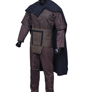 May include: A brown and black costume with a black cape. The costume has a quilted design and a belt with a rectangular buckle.