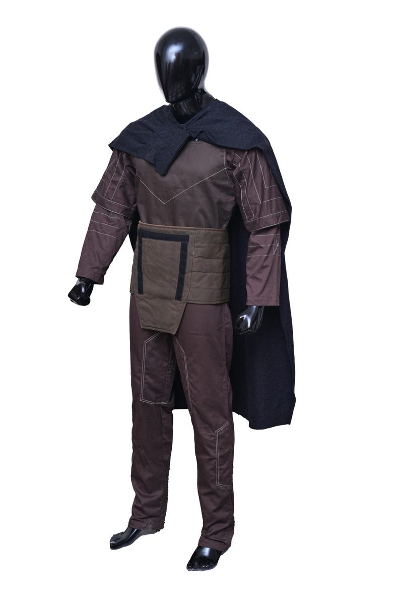 May include: A brown and black costume with a black cape. The costume has a quilted design and a belt with a rectangular buckle.