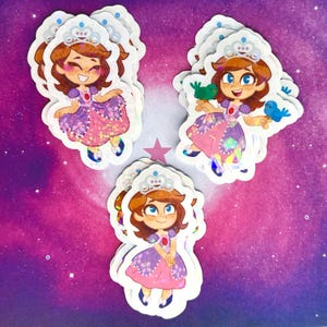 Może przedstawiać: Kolekcja naklejek przedstawiających kreskówkową księżniczkę w różowo-fioletowej sukience, srebrnej tiarze i brązowych włosach. Niektóre naklejki przedstawiają księżniczkę z ptakami. Naklejki mają efekt holograficzny.