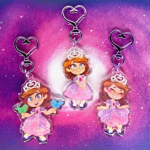 Può includere: Tre portachiavi in acrilico trasparente con una principessa dei cartoni animati in un abito rosa e una tiara. Ogni portachiavi ha una chiusura argentata a forma di cuore. La principessa ha i capelli castani e gli occhi azzurri. Un portachiavi ha la principessa che tiene due uccelli.