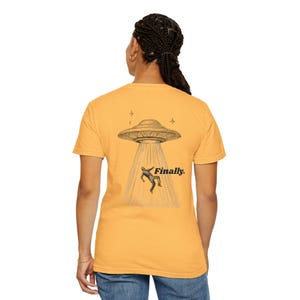 Op de afbeelding: Mosterdgeel T-shirt met een zwart-wit illustratie van een UFO die een persoon ontvoert. Het woord "Finally." staat eronder gedrukt. Dit casual T-shirt is geschikt voor dagelijks gebruik.
