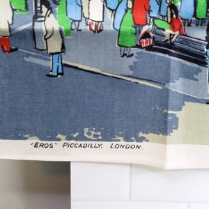 Puede incluir: Un pa&ntilde;o de cocina de tela blanca con una colorida ilustraci&oacute;n gr&aacute;fica de personas en una plaza de la ciudad. La escena incluye figuras con abrigos y el texto "EROS" PICCADILLY, LONDON. impreso en negro en la esquina inferior izquierda.