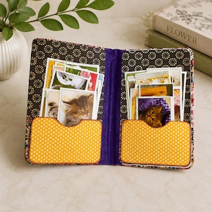 May include: A fabric photo organizer featuring a black interior with a gold circular pattern and two orange pockets with white polka dots. The organizer is filled with numerous small rectangular photographs of kittens and various outdoor scenes.