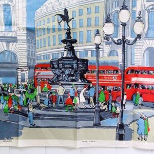 Puede incluir: Un pa&ntilde;o de cocina de recuerdo con una ilustraci&oacute;n colorida de la estatua de Eros en Piccadilly Circus, Londres. La escena incluye autobuses rojos de dos pisos, farolas y peatones. El texto inferior dice Eros Piccadilly London.