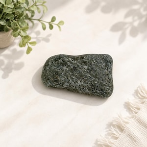 Peut inclure: Une pierre vert foncé lisse avec une surface texturée et tachetée présentant de subtiles inclusions minérales blanches et grises. La pierre a une forme rectangulaire arrondie irrégulière avec des bords polis et un aspect naturel.