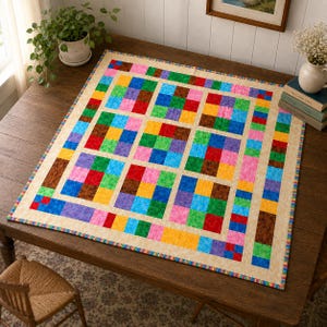 Peut inclure: Une courtepointe carrée composée d'une grille de carrés de tissu multicolores dans des tons de rouge, bleu, vert, jaune, rose et marron. La courtepointe présente une bordure beige clair et un fin liseré à motifs, posée sur une table en bois.