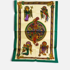 Puede incluir: Un textil rectangular con un centro de color crema y un medall&oacute;n circular central que contiene intrincados motivos de nudos y animales. Cuatro figuras aladas est&aacute;n situadas en las esquinas, enmarcadas por un borde de color verde oscuro y dorado.