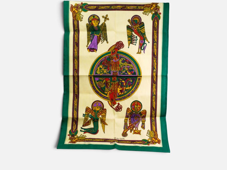 Puede incluir: Un textil rectangular con un centro de color crema y un medall&oacute;n circular central que contiene intrincados motivos de nudos y animales. Cuatro figuras aladas est&aacute;n situadas en las esquinas, enmarcadas por un borde de color verde oscuro y dorado.