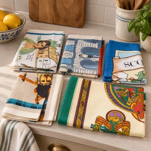 Puede incluir: Una colecci&oacute;n de cinco pa&ntilde;os de cocina rectangulares plegados con varios dise&ntilde;os impresos, incluyendo una persona cerca de un edificio, un arco arquitect&oacute;nico, una pancarta azul con el texto SCO, un gaitero y una colorida ilustraci&oacute;n de estilo celta.