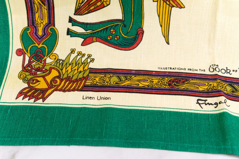 Puede incluir: Un tejido de mezcla de lino color crema con un borde verde vibrante e intrincadas ilustraciones de estilo celta. El dise&ntilde;o incluye una criatura verde estilizada, detalles en amarillo y rojo, y el texto "ILLUSTRATIONS FROM THE BOOK OF" y "Fingal".