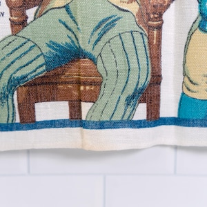 Puede incluir: Un pa&ntilde;o de cocina de tela blanca con una ilustraci&oacute;n impresa de figuras con ropa de &eacute;poca, incluida una persona con pantalones de rayas verdes sentada en una silla de madera marr&oacute;n. El texto SOUTER JOHNNY est&aacute; impreso en negro arriba a la izquierda.