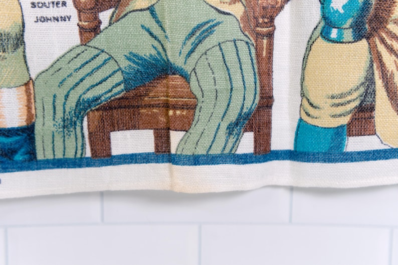 Puede incluir: Un pa&ntilde;o de cocina de tela blanca con una ilustraci&oacute;n impresa de figuras con ropa de &eacute;poca, incluida una persona con pantalones de rayas verdes sentada en una silla de madera marr&oacute;n. El texto SOUTER JOHNNY est&aacute; impreso en negro arriba a la izquierda.