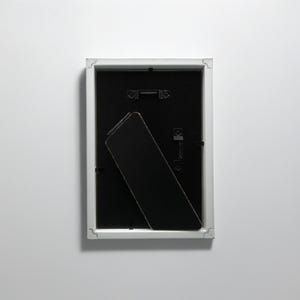 May include: White picture frame with a black mat and a black easel stand on the back.