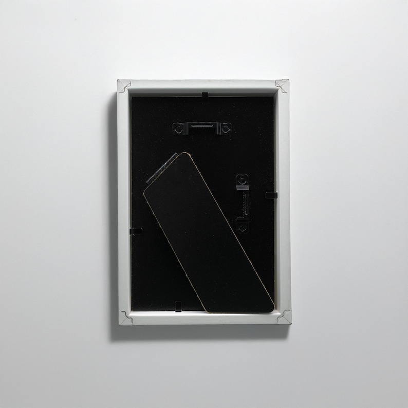 May include: White picture frame with a black mat and a black easel stand on the back.