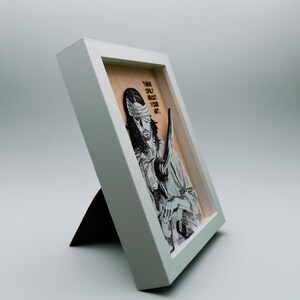 May include: A framed wood print of a character with a blindfold and a sword, with the text "Think only about your art."