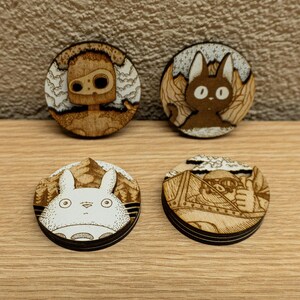 Set of four handcrafted wooden magnets inspired by Studio Ghibli films — Totoro, Porco Rosso, Jiji, and the guardian robot from Castle in the Sky. Each magnet features detailed laser engraving on layered plywood and MDF, with warm natural tones. Displayed on a wooden surface, highlighting their smooth finish and sturdy build. Perfect collectible or gift for anime and Studio Ghibli fans.